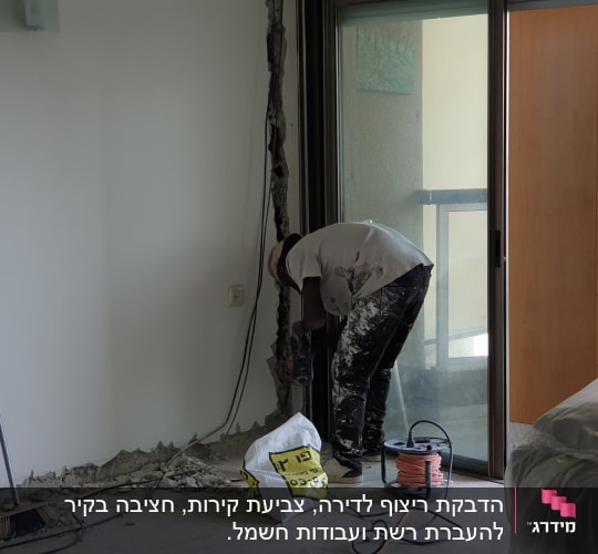 עובד קודח בקיר עם מקדחה חשמלית, כבלים על הרצפה